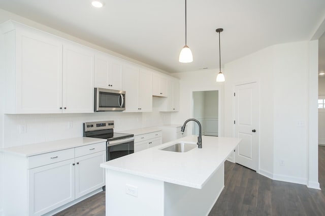 kitchen with pendant lighting, stainless steel appliances, a center island with sink, and white cabinets