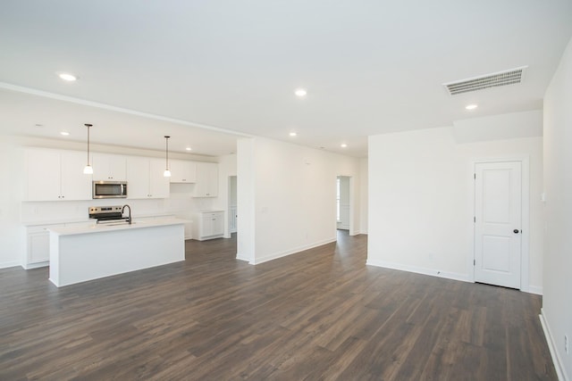 kitchen featuring appliances with stainless steel finishes, dark hardwood / wood-style floors, white cabinets, hanging light fixtures, and a kitchen island with sink