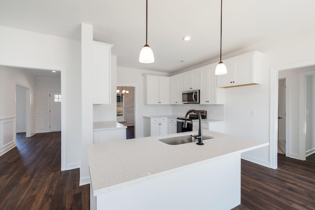 kitchen featuring dark wood-type flooring, pendant lighting, a center island with sink, white cabinets, and appliances with stainless steel finishes