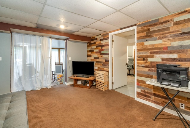 living room featuring carpet flooring, a paneled ceiling, and wood walls