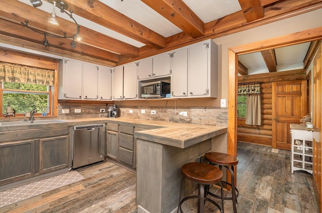 kitchen featuring log walls, dark wood-type flooring, beamed ceiling, stainless steel dishwasher, and decorative backsplash