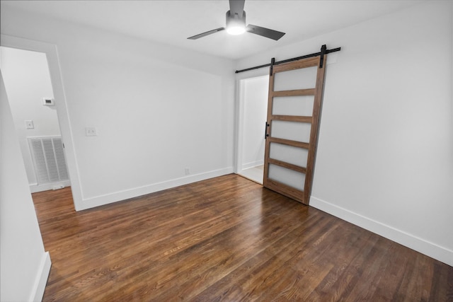 unfurnished bedroom with a barn door, ceiling fan, and dark hardwood / wood-style flooring