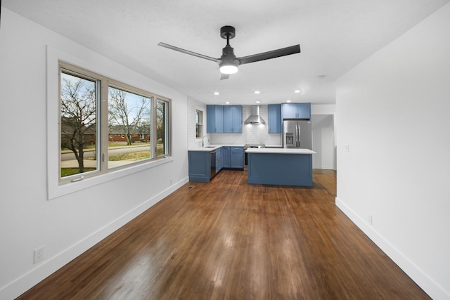 interior space with backsplash, blue cabinets, sink, wall chimney exhaust hood, and stainless steel appliances