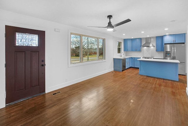 kitchen featuring blue cabinets, sink, wall chimney exhaust hood, decorative backsplash, and stainless steel appliances