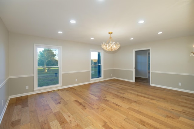 unfurnished room featuring a notable chandelier and light wood-type flooring