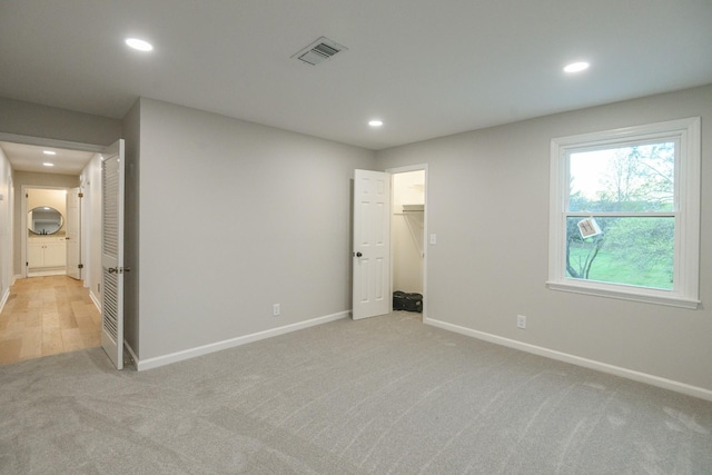 unfurnished bedroom with a spacious closet, a closet, and light colored carpet