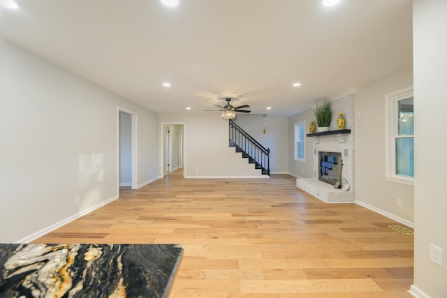 living room featuring ceiling fan, a large fireplace, a healthy amount of sunlight, and light wood-type flooring