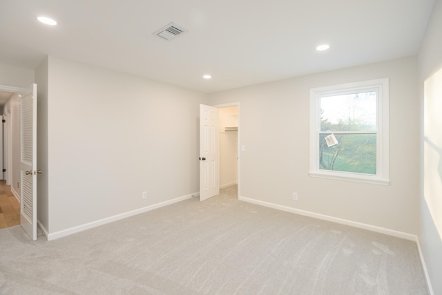 unfurnished bedroom featuring a walk in closet, light colored carpet, and a closet