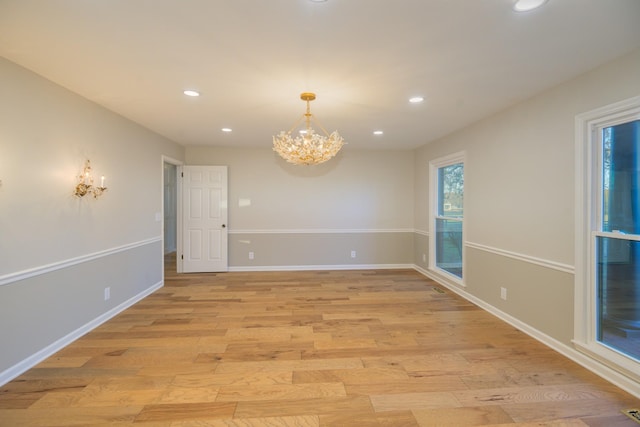 spare room featuring light wood-type flooring and a chandelier