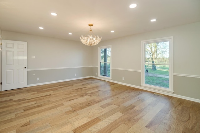 spare room featuring plenty of natural light, light hardwood / wood-style floors, and an inviting chandelier