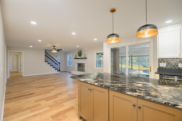 kitchen featuring dark stone counters, a large fireplace, ceiling fan, pendant lighting, and light hardwood / wood-style floors