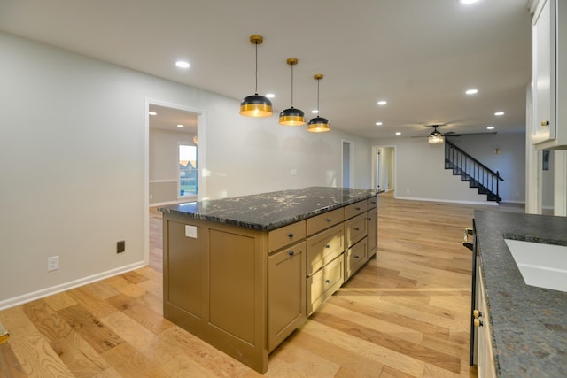 kitchen with dark stone counters, a kitchen island, hanging light fixtures, and light wood-type flooring