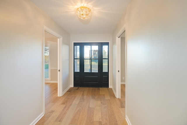 doorway to outside with a notable chandelier and light wood-type flooring