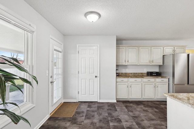 kitchen featuring white cabinetry, stainless steel refrigerator, light stone counters, and a textured ceiling