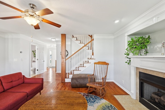 living room featuring ceiling fan, light hardwood / wood-style floors, crown molding, and a tiled fireplace