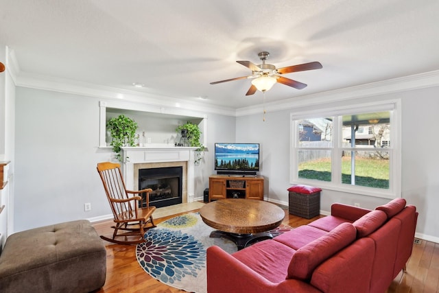 living room featuring hardwood / wood-style floors, ceiling fan, ornamental molding, and a tiled fireplace