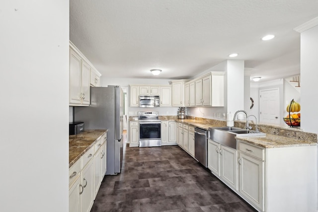 kitchen with sink, light stone counters, kitchen peninsula, white cabinets, and appliances with stainless steel finishes