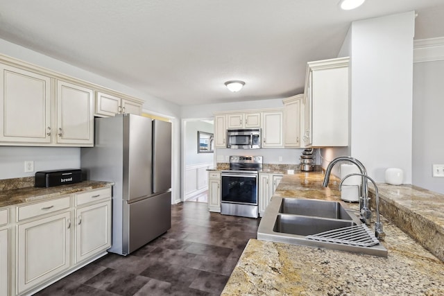 kitchen with light stone countertops, cream cabinets, sink, and stainless steel appliances