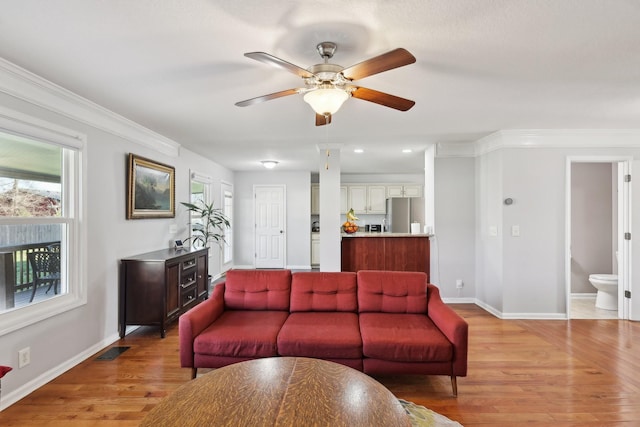 living room with light wood-type flooring, a wealth of natural light, ornamental molding, and ceiling fan