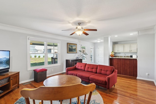 living room featuring ceiling fan, sink, light hardwood / wood-style floors, and ornamental molding