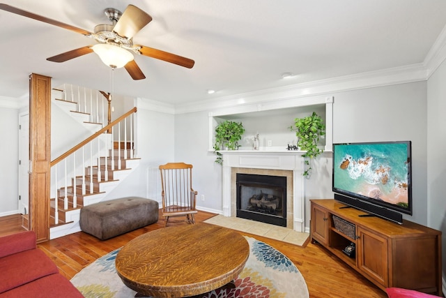 living room with crown molding, a fireplace, ceiling fan, and light wood-type flooring