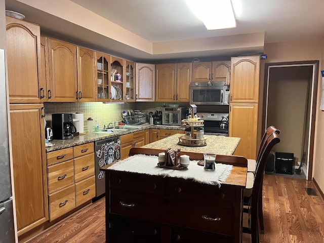 kitchen featuring hardwood / wood-style flooring, a center island, backsplash, and appliances with stainless steel finishes