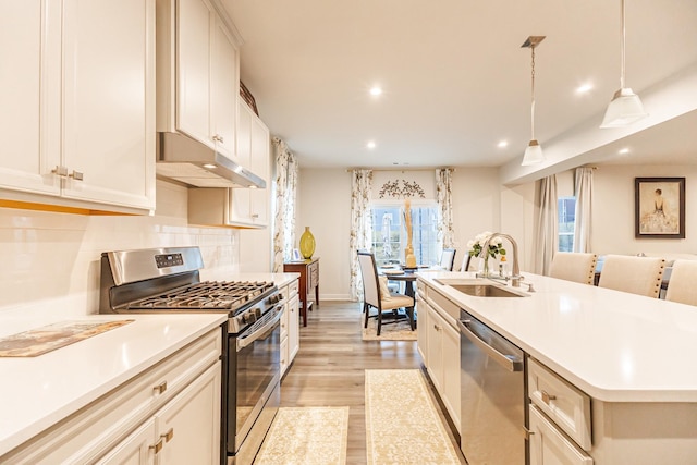 kitchen featuring an island with sink, sink, decorative backsplash, hanging light fixtures, and stainless steel appliances