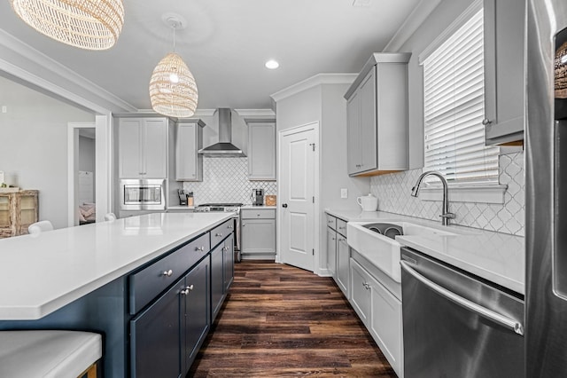 kitchen featuring hanging light fixtures, wall chimney range hood, a kitchen bar, gray cabinets, and appliances with stainless steel finishes