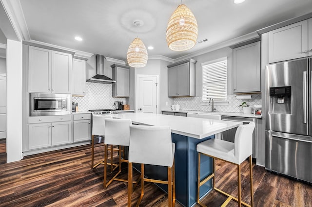 kitchen featuring stainless steel appliances, wall chimney range hood, gray cabinets, a kitchen island, and hanging light fixtures