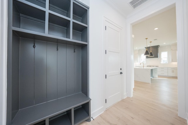 mudroom featuring built in shelves, crown molding, sink, and light hardwood / wood-style floors