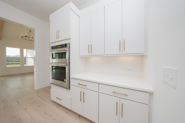 kitchen with white cabinetry, an inviting chandelier, tasteful backsplash, light hardwood / wood-style flooring, and double oven