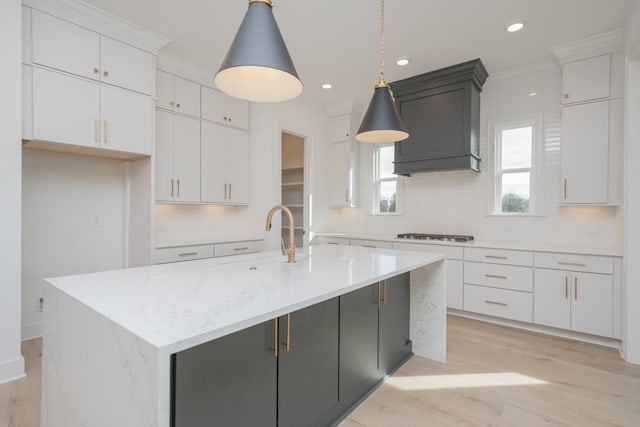 kitchen featuring custom range hood, sink, pendant lighting, a center island with sink, and white cabinets