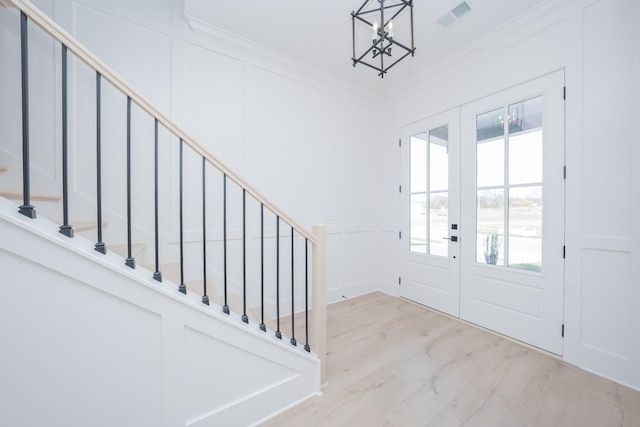 entrance foyer with light hardwood / wood-style floors, ornamental molding, french doors, and a chandelier