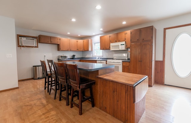 kitchen featuring a center island, sink, a wall unit AC, light hardwood / wood-style floors, and white appliances