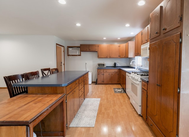 kitchen with sink, a wall mounted air conditioner, white appliances, a breakfast bar area, and light wood-type flooring