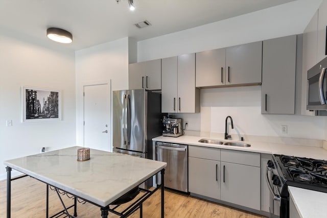 kitchen with appliances with stainless steel finishes, light hardwood / wood-style floors, gray cabinetry, and sink