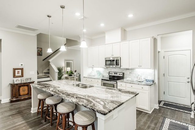 kitchen featuring white cabinets, stainless steel appliances, hanging light fixtures, and an island with sink