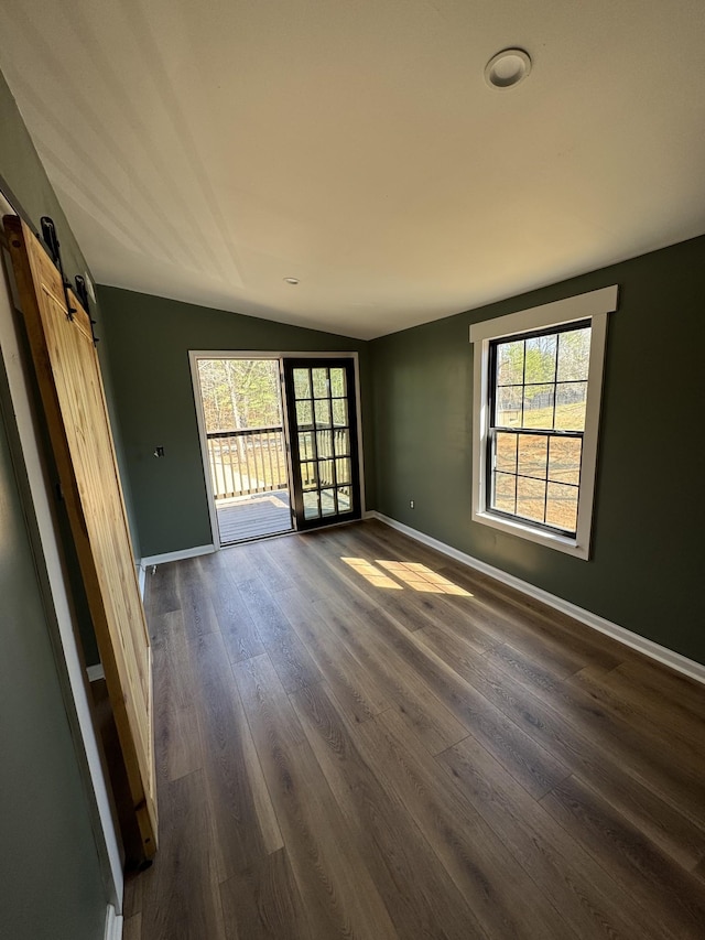 unfurnished room with baseboards, lofted ceiling, a barn door, and dark wood-style flooring