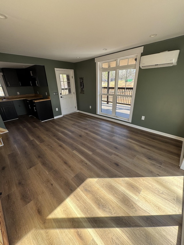 unfurnished living room featuring dark wood-style floors, baseboards, and a wall mounted air conditioner