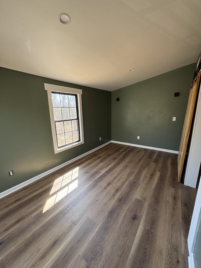 unfurnished room featuring dark wood-style floors, baseboards, and a barn door