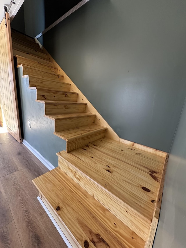 stairway with a barn door and wood finished floors