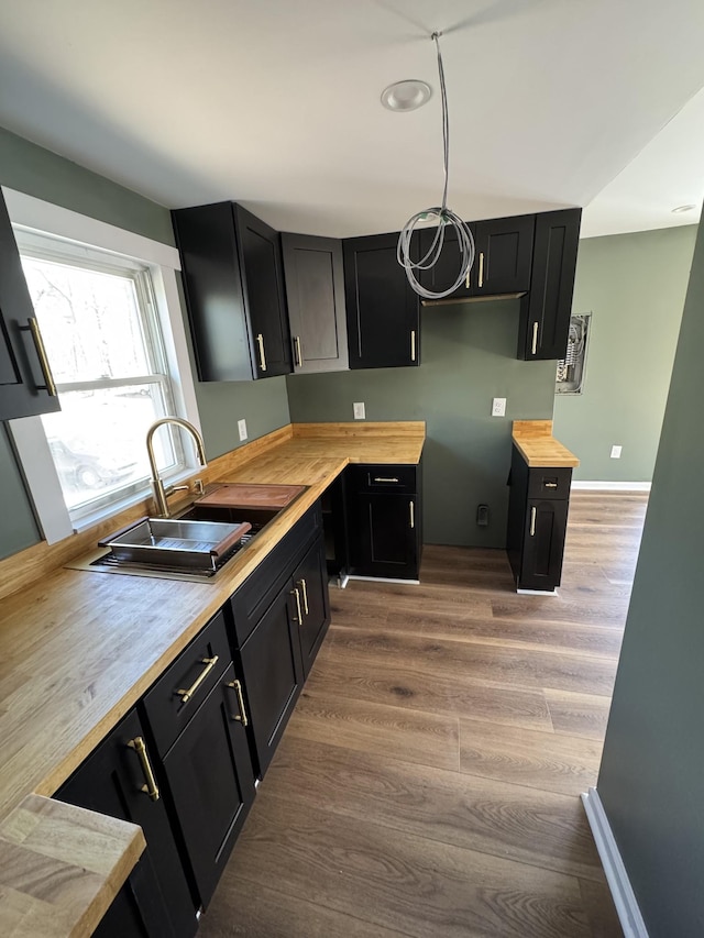 kitchen featuring dark cabinetry, butcher block countertops, wood finished floors, and a sink