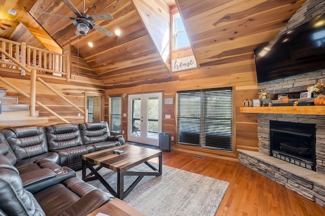 living room featuring ceiling fan, french doors, wood walls, a fireplace, and light wood-type flooring