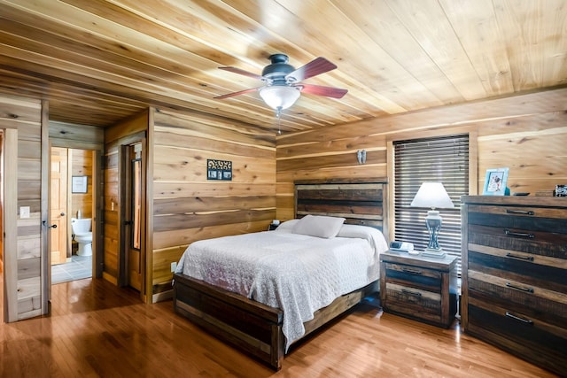 bedroom with ceiling fan, light hardwood / wood-style flooring, wooden ceiling, connected bathroom, and wood walls