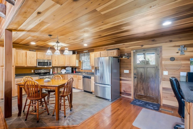 kitchen featuring appliances with stainless steel finishes, wood ceiling, wooden walls, light brown cabinets, and decorative light fixtures