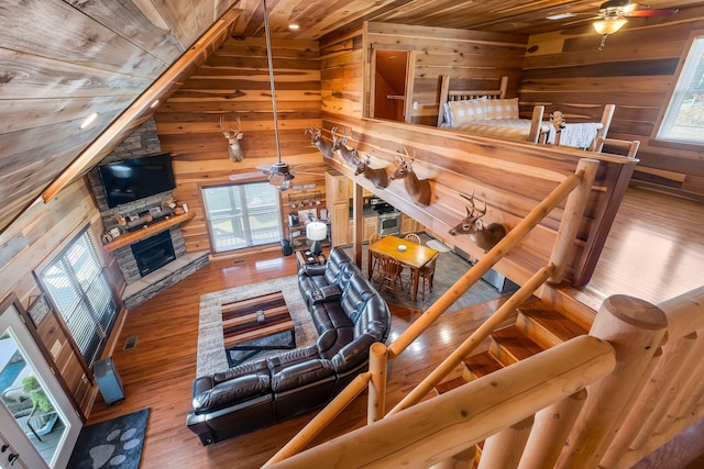 living room with wood ceiling, ceiling fan, hardwood / wood-style flooring, a stone fireplace, and wood walls