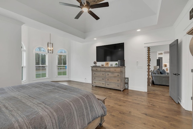 bedroom with a tray ceiling, dark wood-type flooring, and ceiling fan with notable chandelier