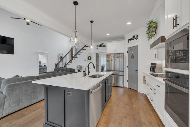 kitchen with pendant lighting, a center island with sink, sink, appliances with stainless steel finishes, and white cabinetry