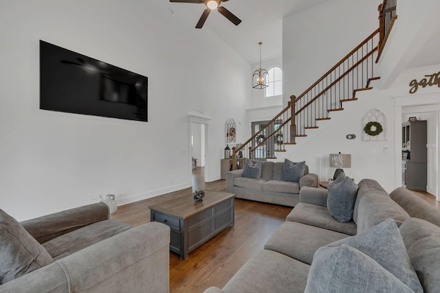 living room featuring a towering ceiling, dark wood-type flooring, and ceiling fan with notable chandelier