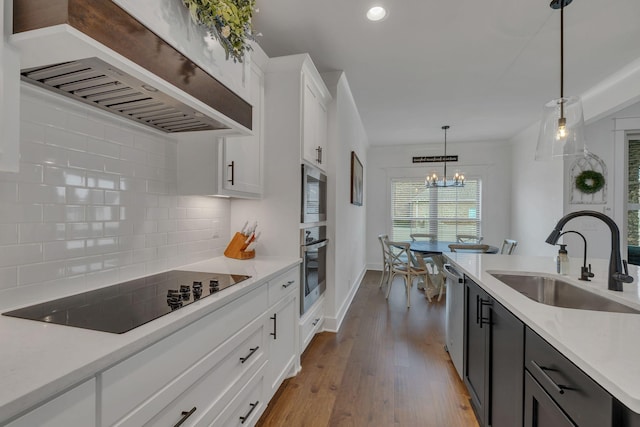 kitchen featuring white cabinetry, sink, wall chimney range hood, tasteful backsplash, and decorative light fixtures